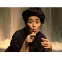 Photograph of Brenda Wong Aoki expressively looking into the camera and pointing. Her hair is piled on top of her head in a loose bun.